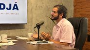 Túlio Gadelha fala em microfone sentado. Ao fundo TV com a logo do PodJá
