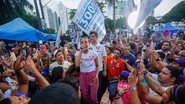 Raquel Lyra fala em microfone ao redor de multidão. Eduardo da Fonte está atrás dela. Todos em pé. Ao redor bandeiras