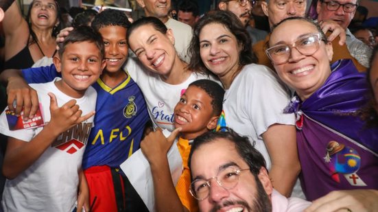Raquel Lyra posa para foto ao lado de várias pessoas sorrindo, entre elas 3 crianças negras. Também sorriem Túlio Gadelha e Priscila Krause