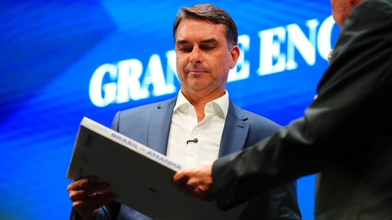 Imagem mostra foto do senador Flávio Bolsonaro de cabeça baixo, com aspecto sério, segurando um livro