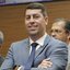 Imagem mostra o vereador Samuel Salazar de terno cinza sorridente na Câmara de Vereadores