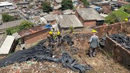 Encosta com lona e lixo vista de cima. pedreiros com capacetes amarelos trabalham. abaixo casas