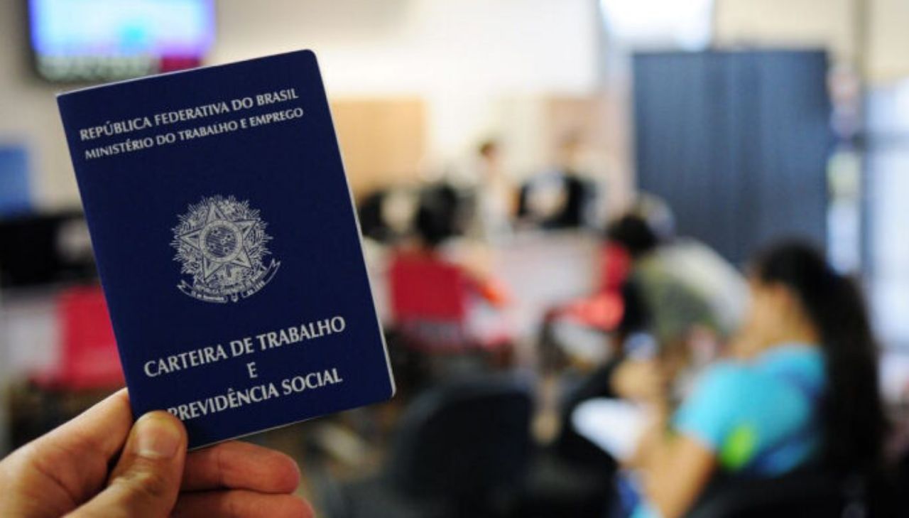 Foto da Carteira de Trabalho em sua verssão impressa, em primeiro plano. O resto do cenário está desfocado, só a carteira de trabalho aparece facada