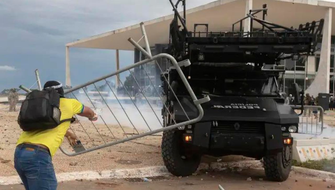 Imagem de homem com a camisa do Brasil jogando uma cerca contra um carro da Polícia, em ato de vandalismo no DF