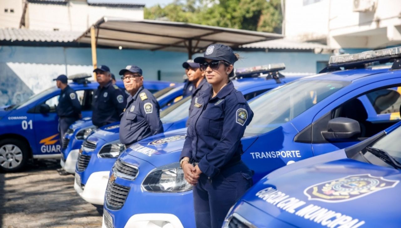 Foto apresentando agendes da Guarda Municipal do Recife, ao lado de viaturas da Guarda Municipal, nas cores azuis