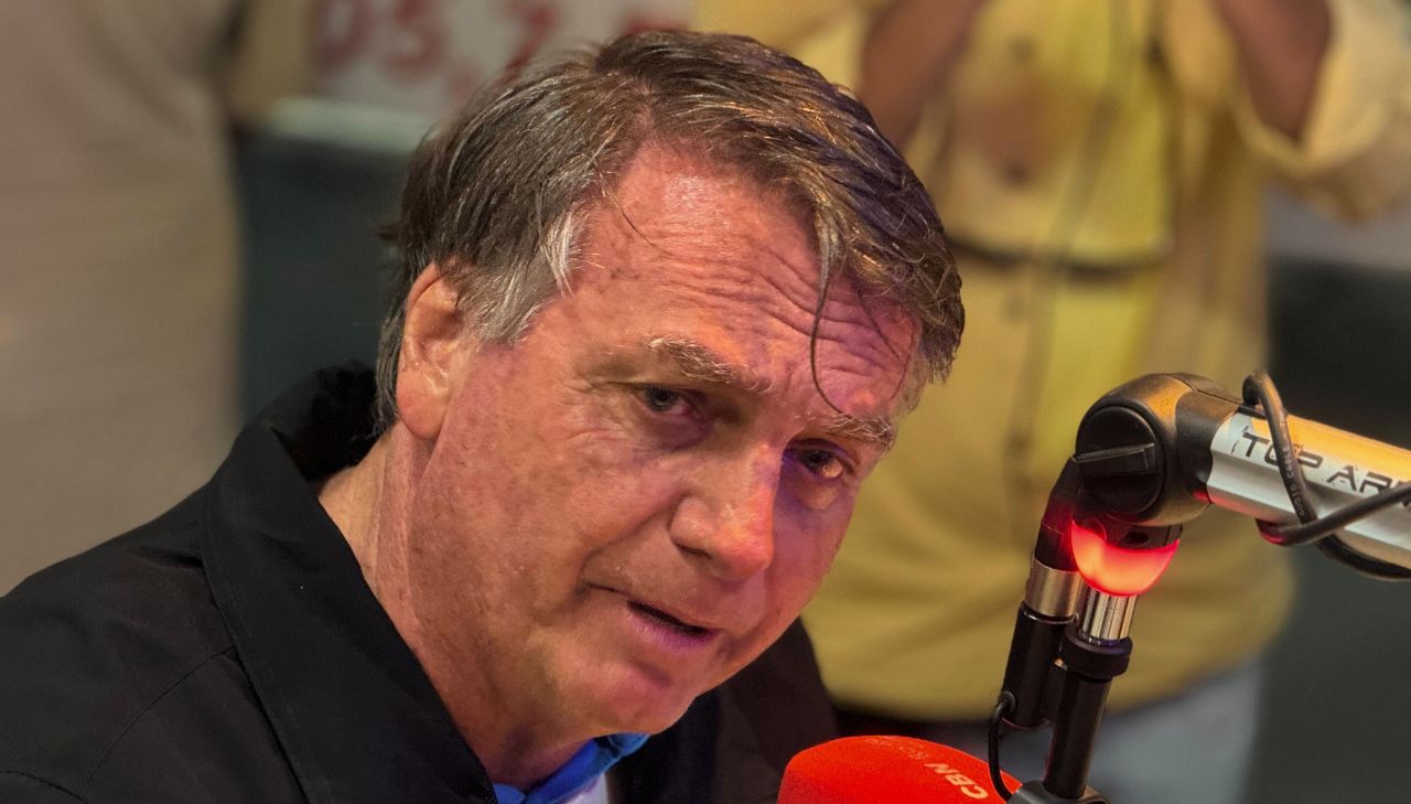 Foto de Bolsonaro falando em um microfone de rádio durante entrevista na rádio CBN, ele olha para lateral