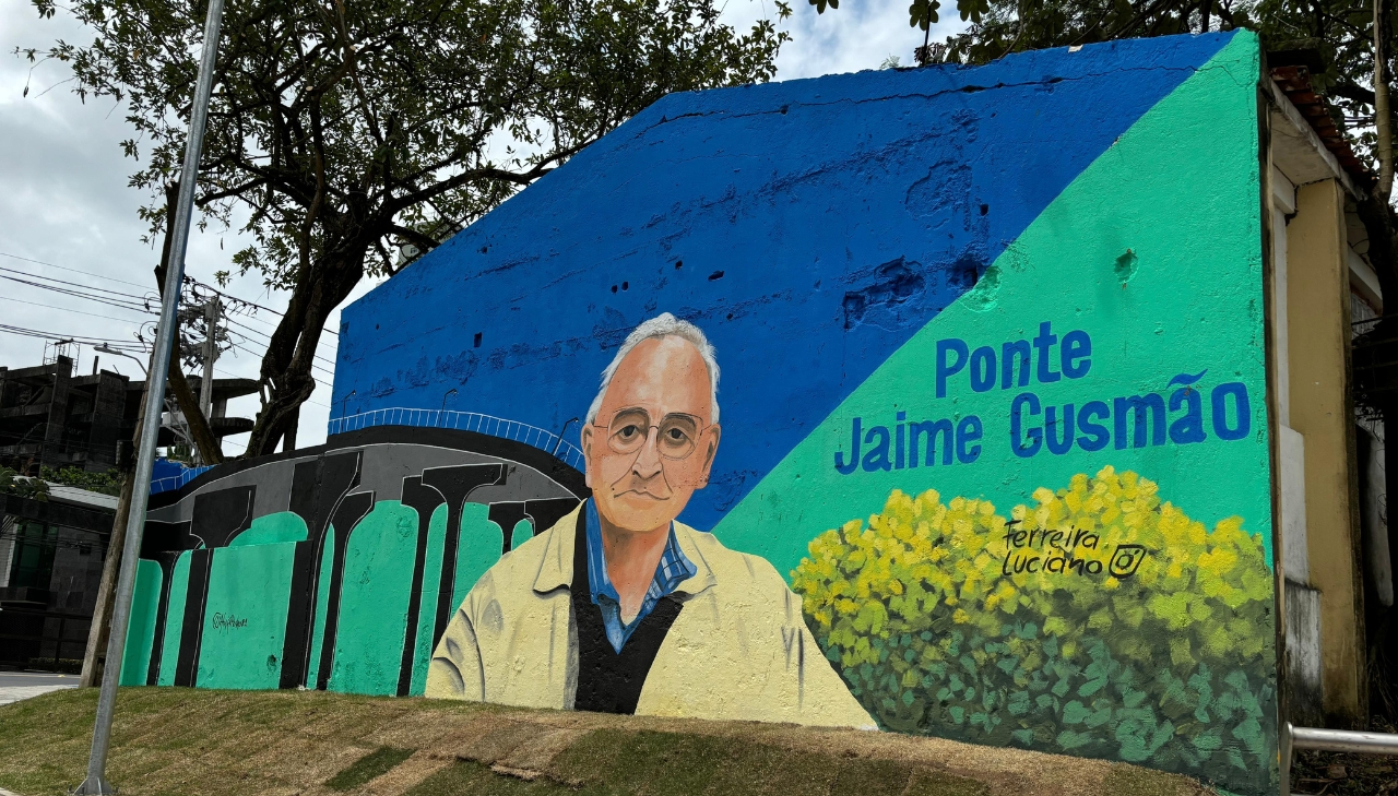 Parede com pintura azul e verde, a imagem de um homem branco de cabelos grisalhos foi desenhada. Está escrito "ponte Jaime Gusmão"