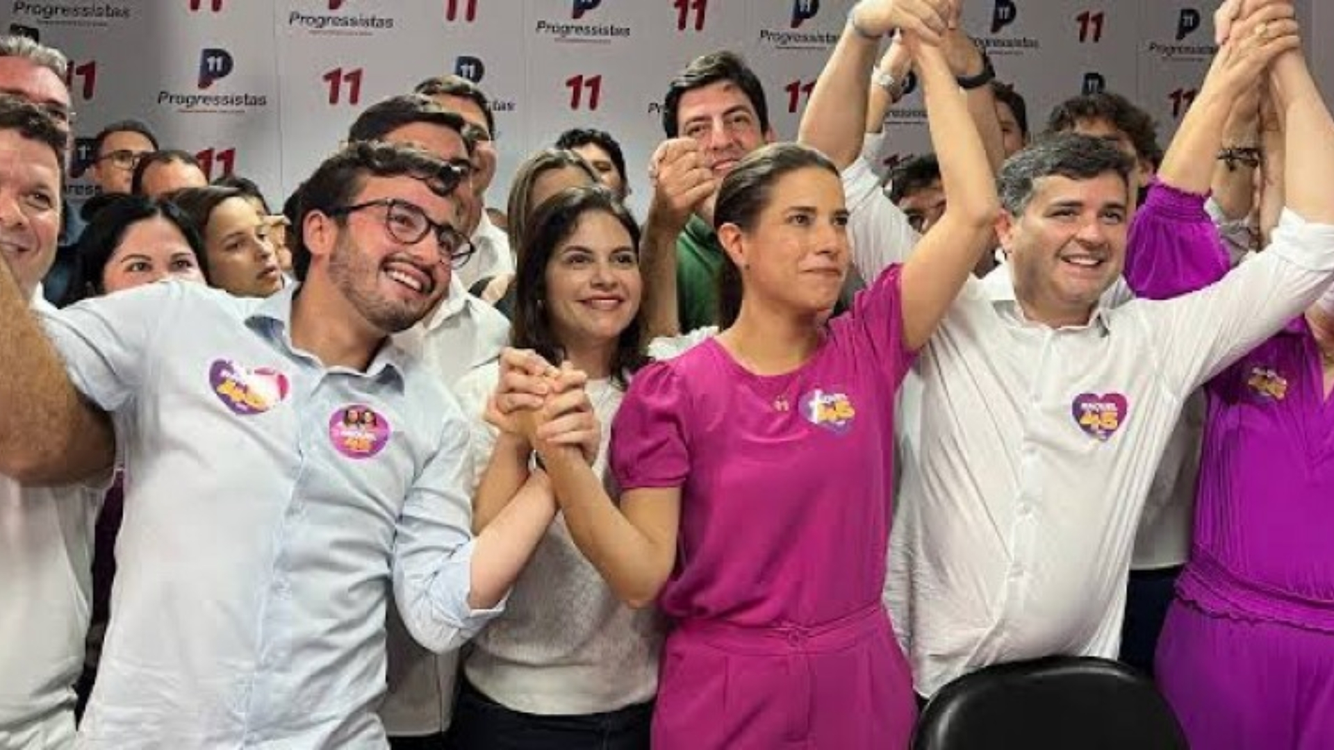 Raquel Lyra, Eduardo da Fonte e Lula da Fonte estão de mãos unidas levantadas com adesivos escrito 45, ao fundo símbolo do PP e o número 11