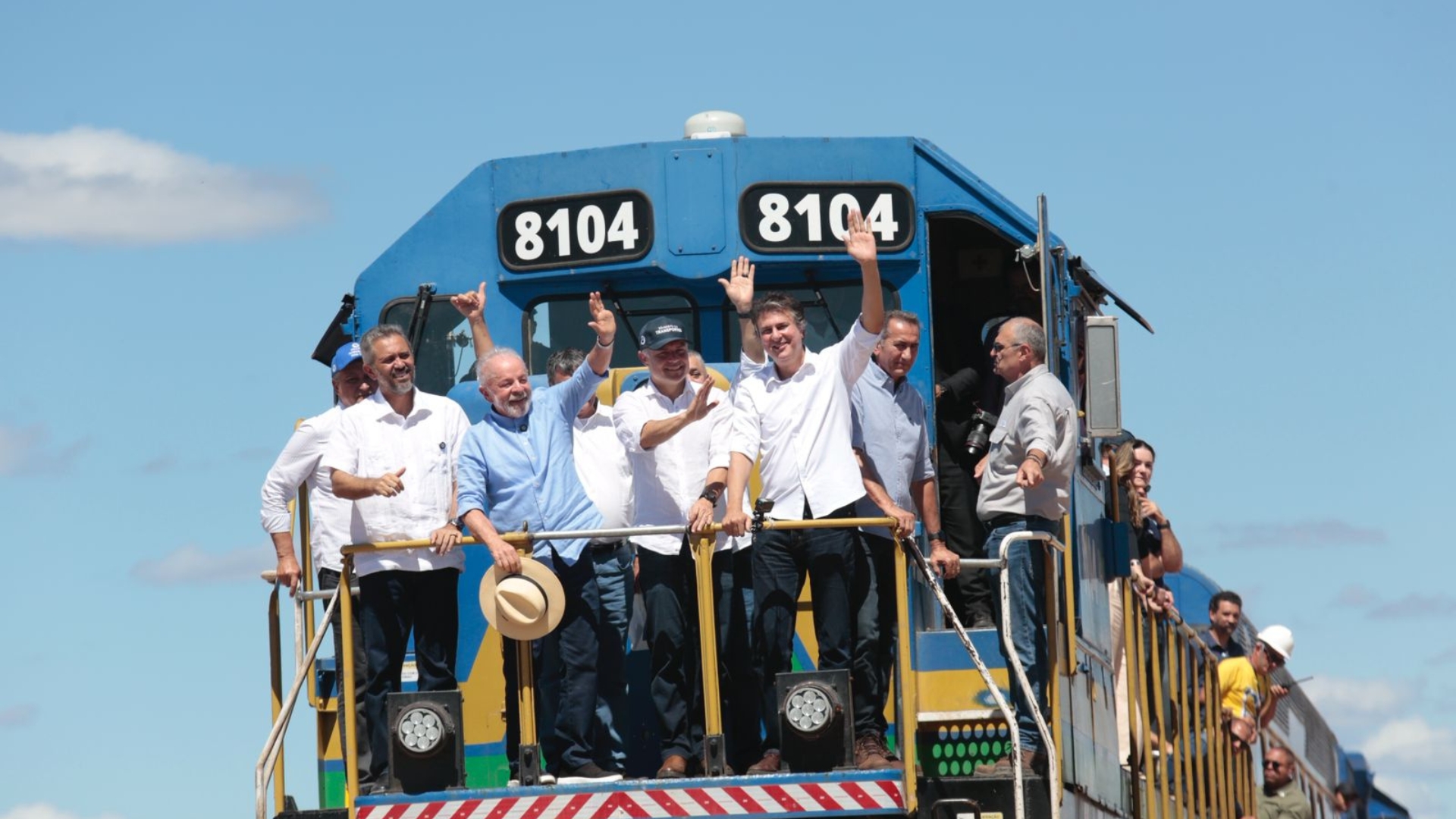 Lula, Camilo Santana e outros homens acenam para epssoas em cima de trem