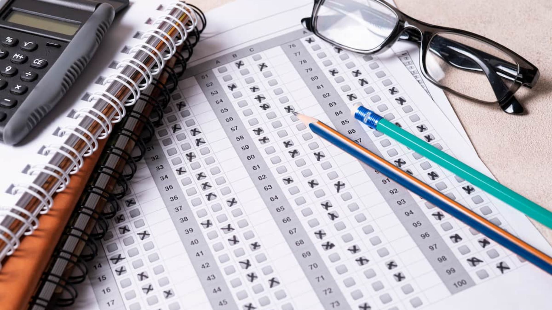Gabarito de prova preenchido ao lado de lápis, caderno, calculadora e um óculos