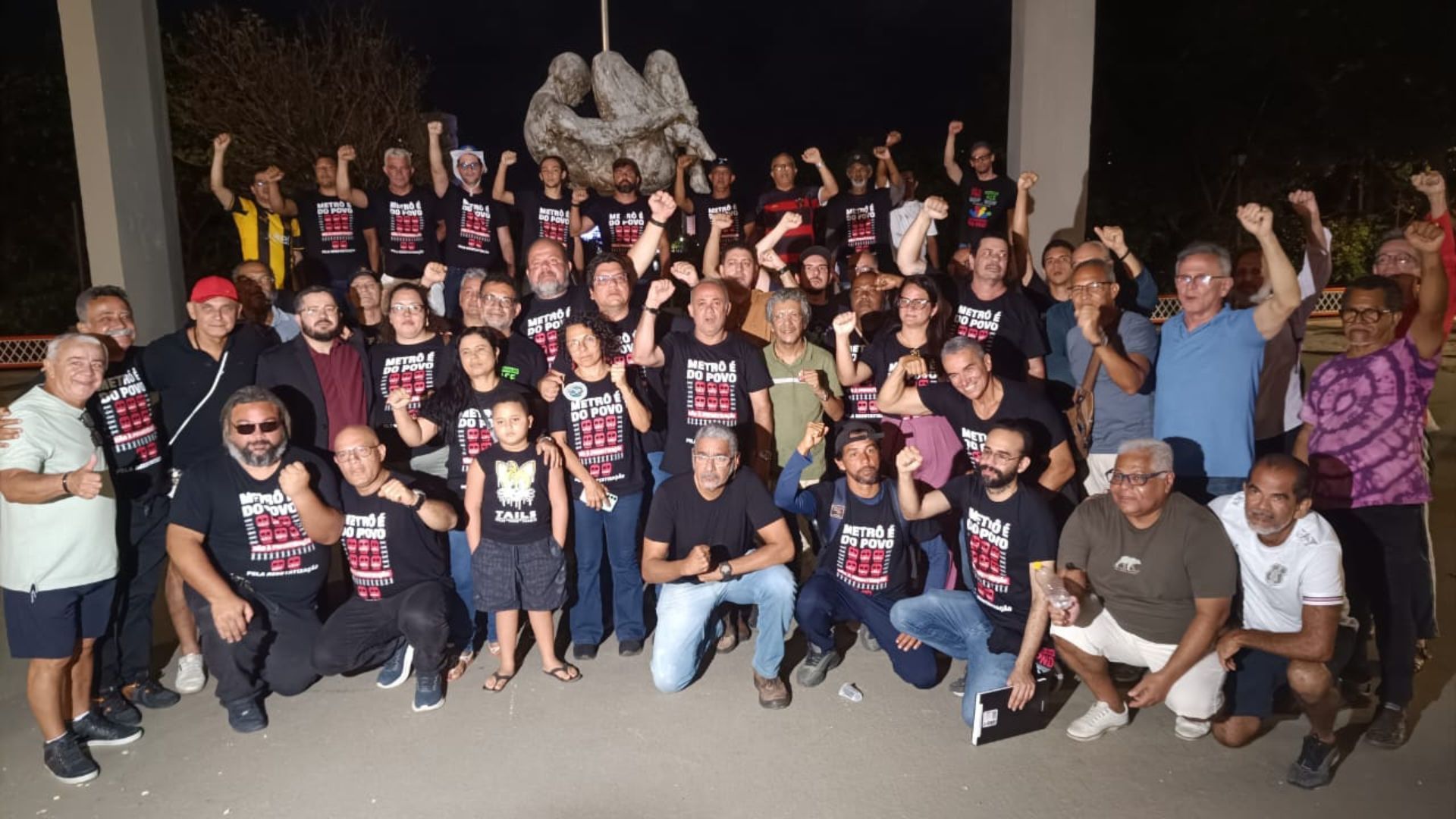 Grupo de pessoas com camisetas pretas escrito "metrô é do povo" com mãos direitas erguidas em punho. Luiz Soares é um deles