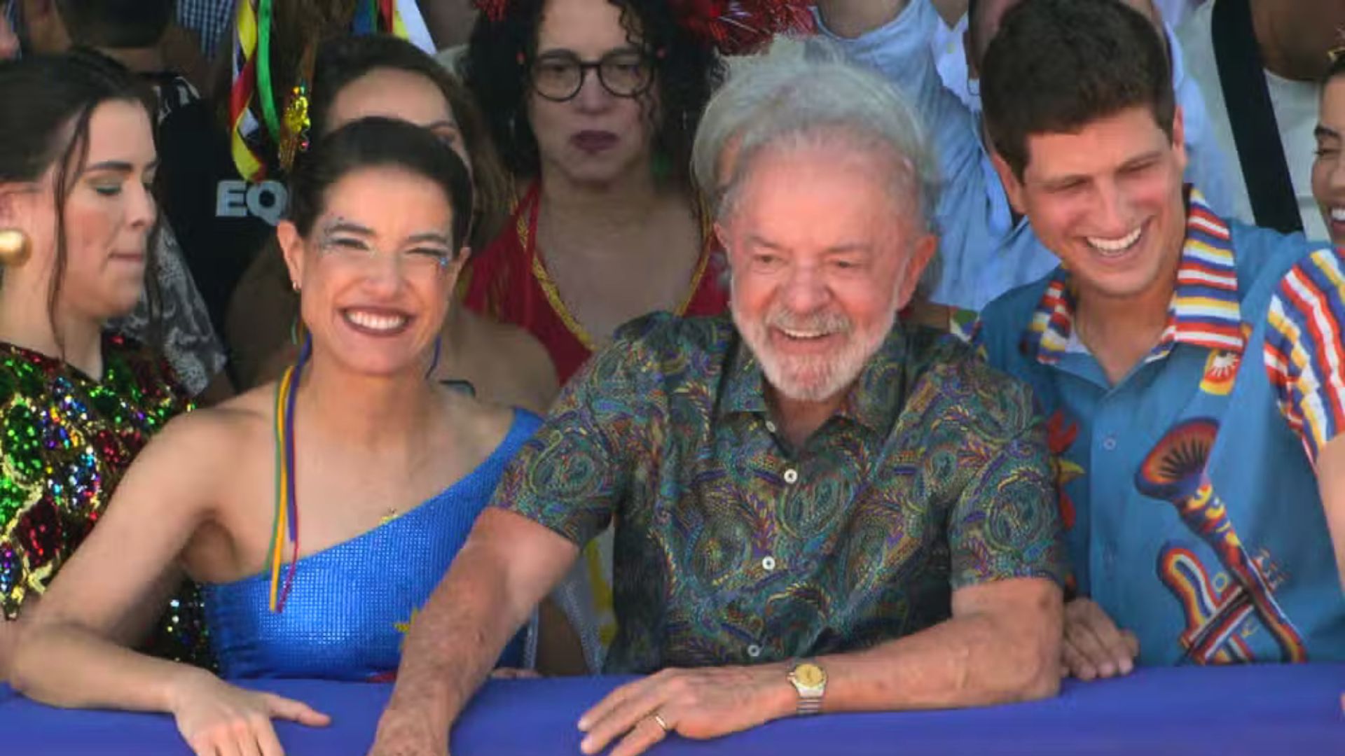 Com roupas carnavalescas sorriem Raquel Lyra, Lula e João Campos. Ao fundo Maria Arraes e Luciana Santos
