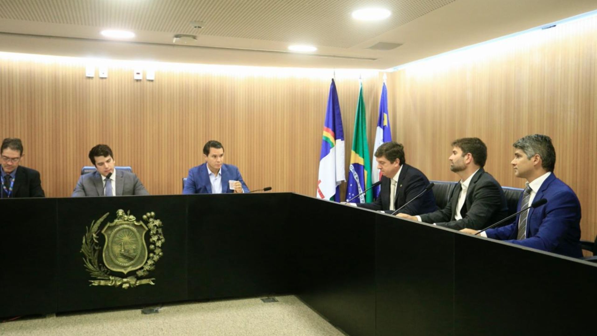 Antonio Coelho, Renato Antunes Gustavo Gouveia João de Nadegi e João de Nadegi sentados em mesa com símbolo da ALEPE, ao fundo bandeiras de Pernambuco, Brasil e Recife