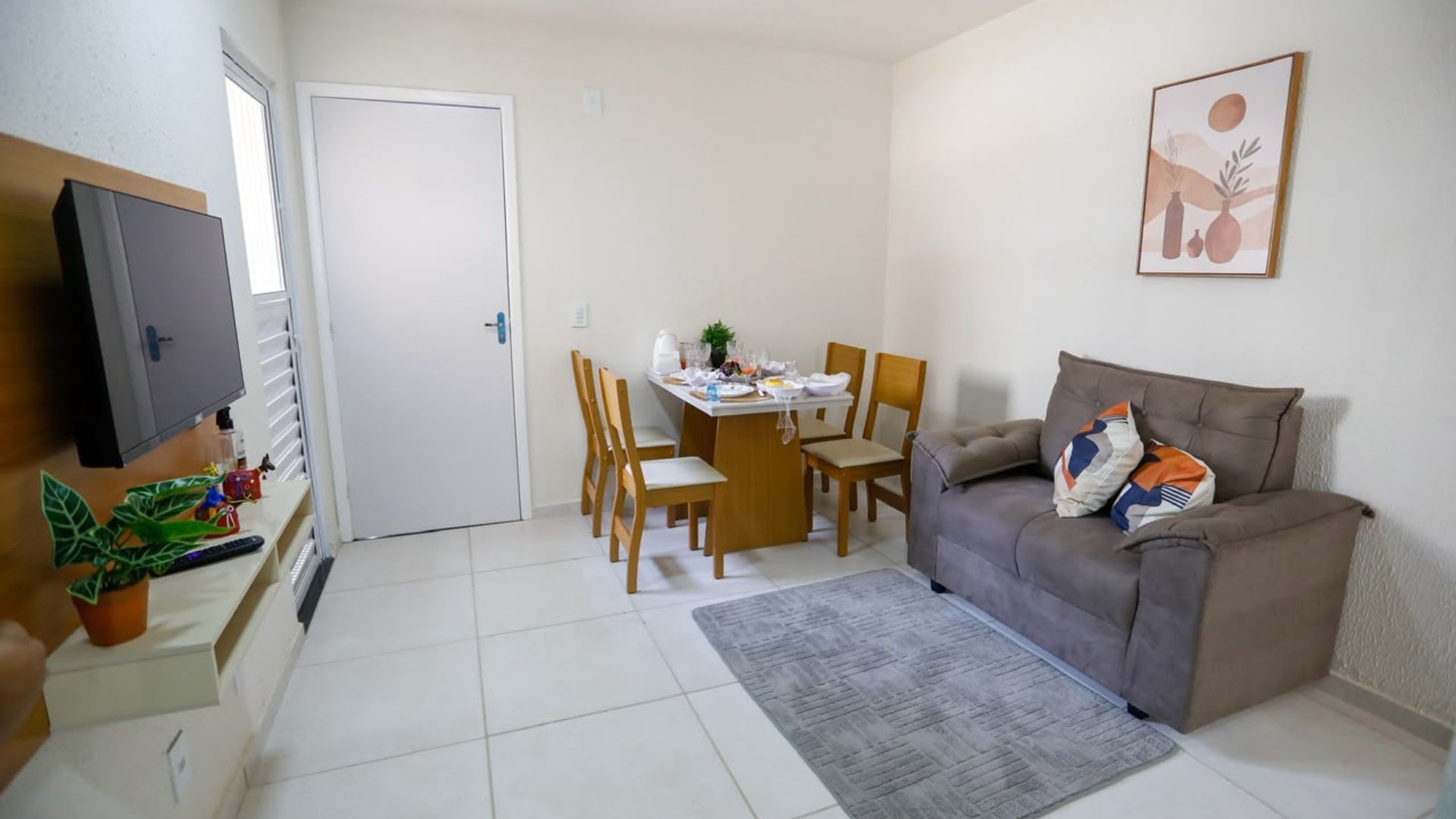 Interior mobiliado de apartamento com piso claro, sofá cinza, televisão e mesa de jantar